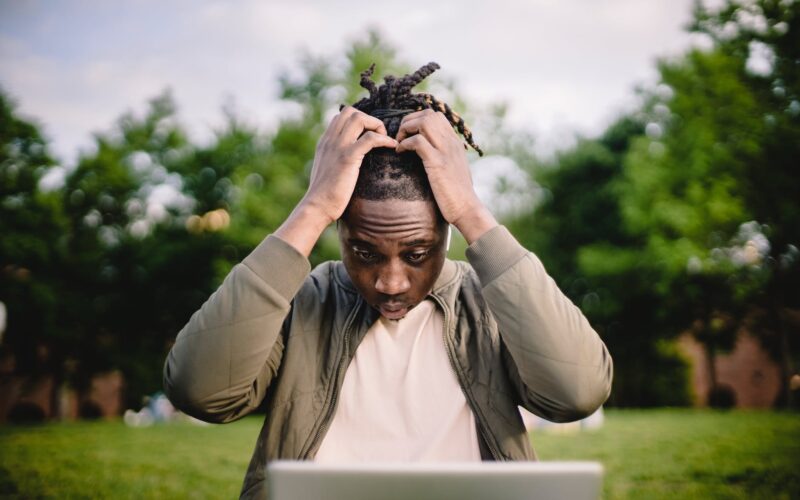 stressed black male entrepreneur working on laptop in park