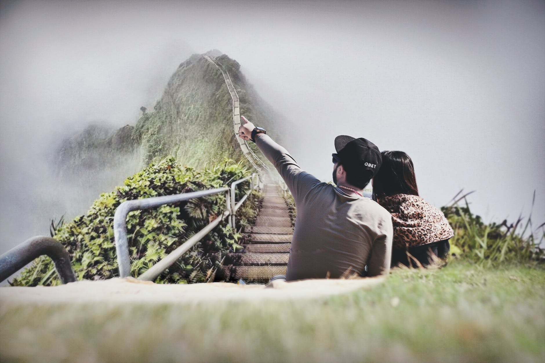 photography of couple sitting on green grass near bridge