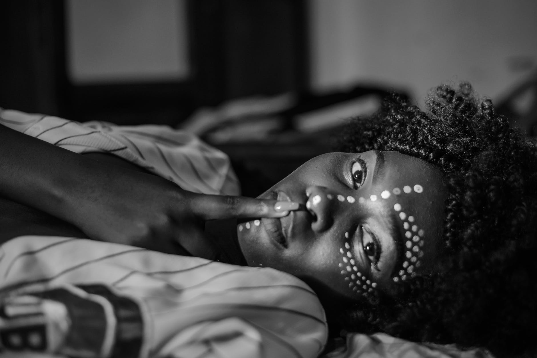 selective focus grayscale photo of women in face paint lying down posing with her finger on her lips