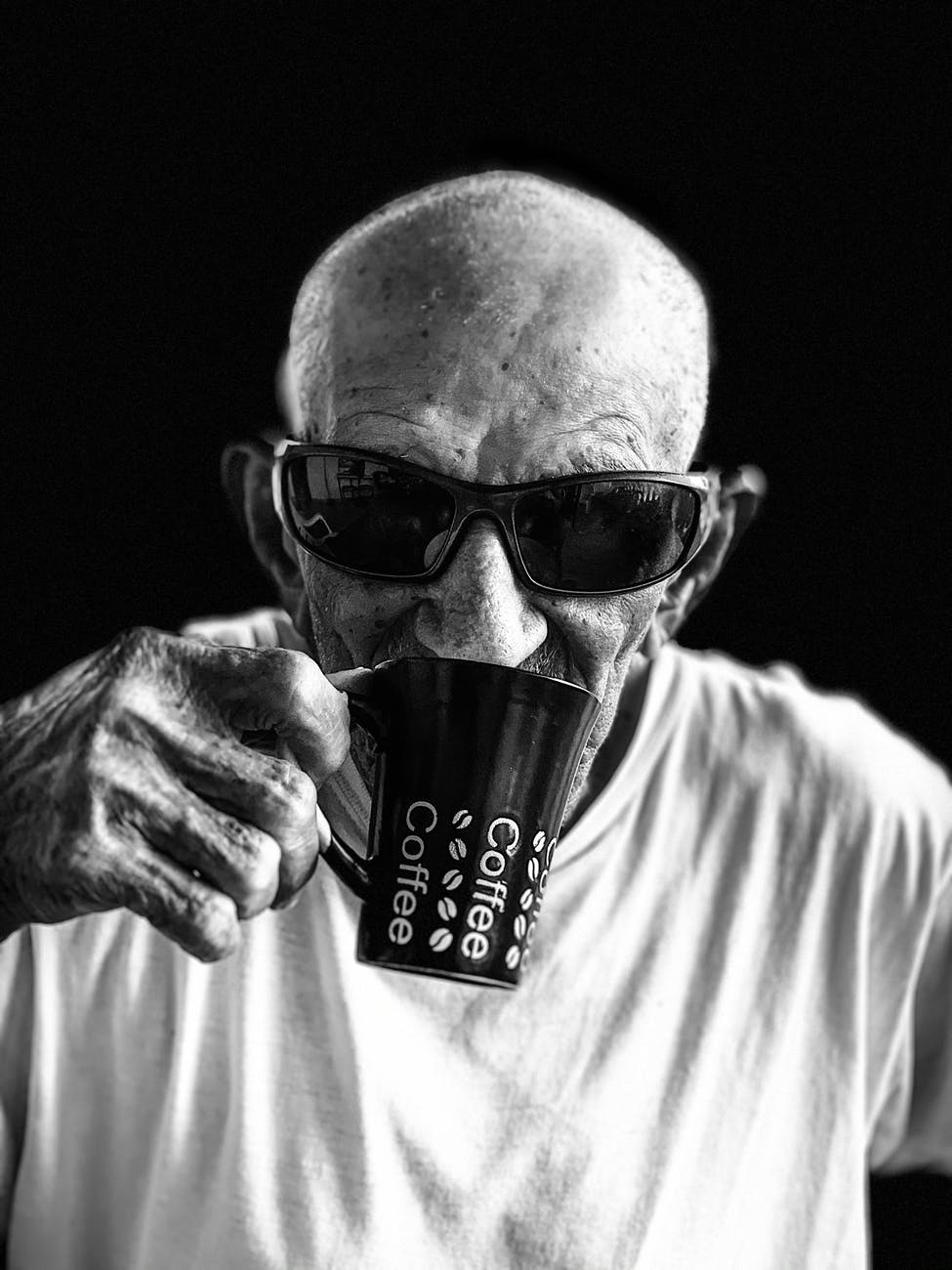 man in white crew neck shirt wearing black sunglasses holding black ceramic mug