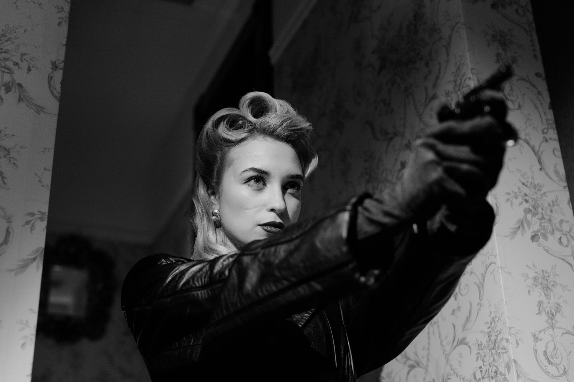 blonde woman in black leather coat pointing a gun