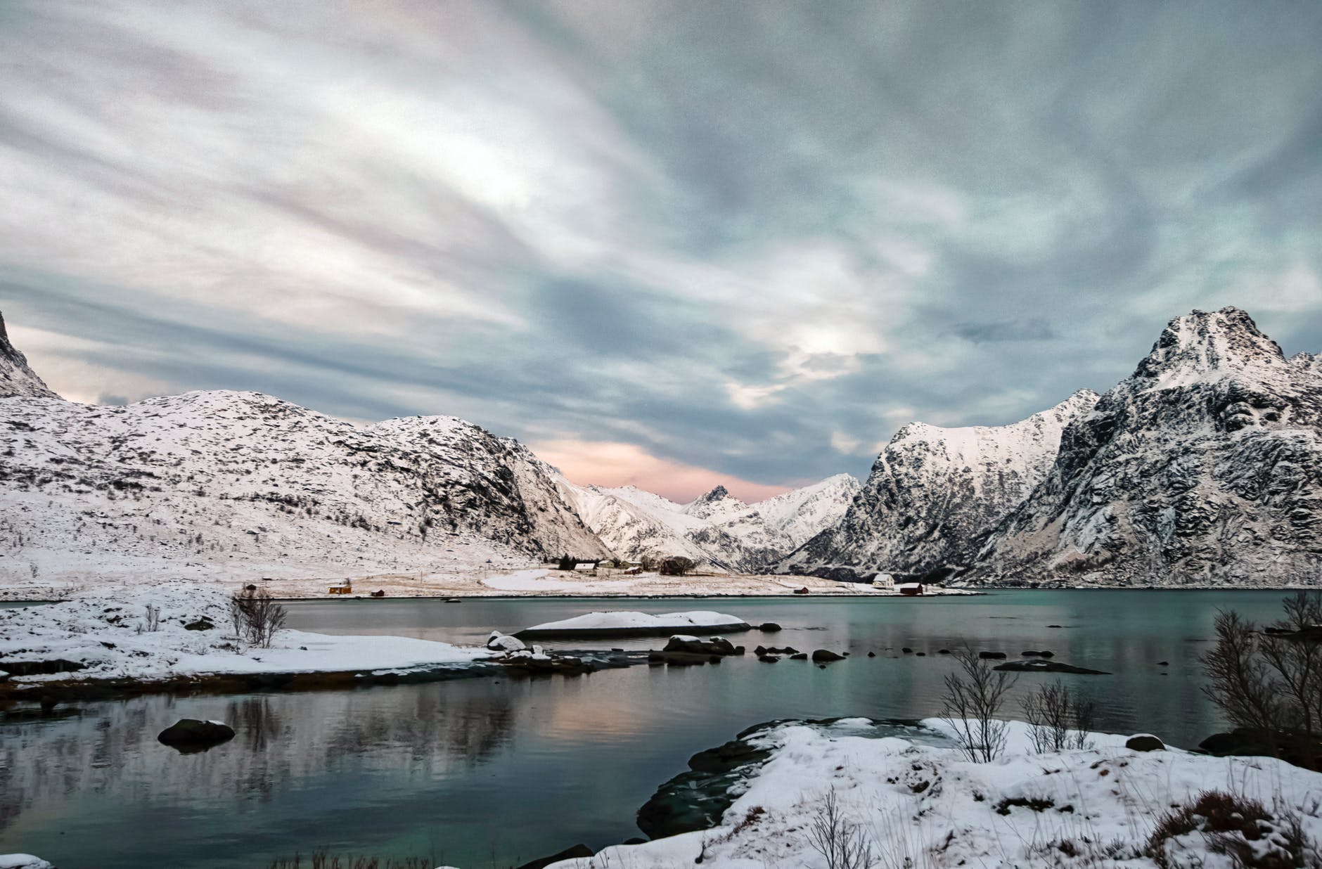 snow covered mountain near lake under cloudy sky