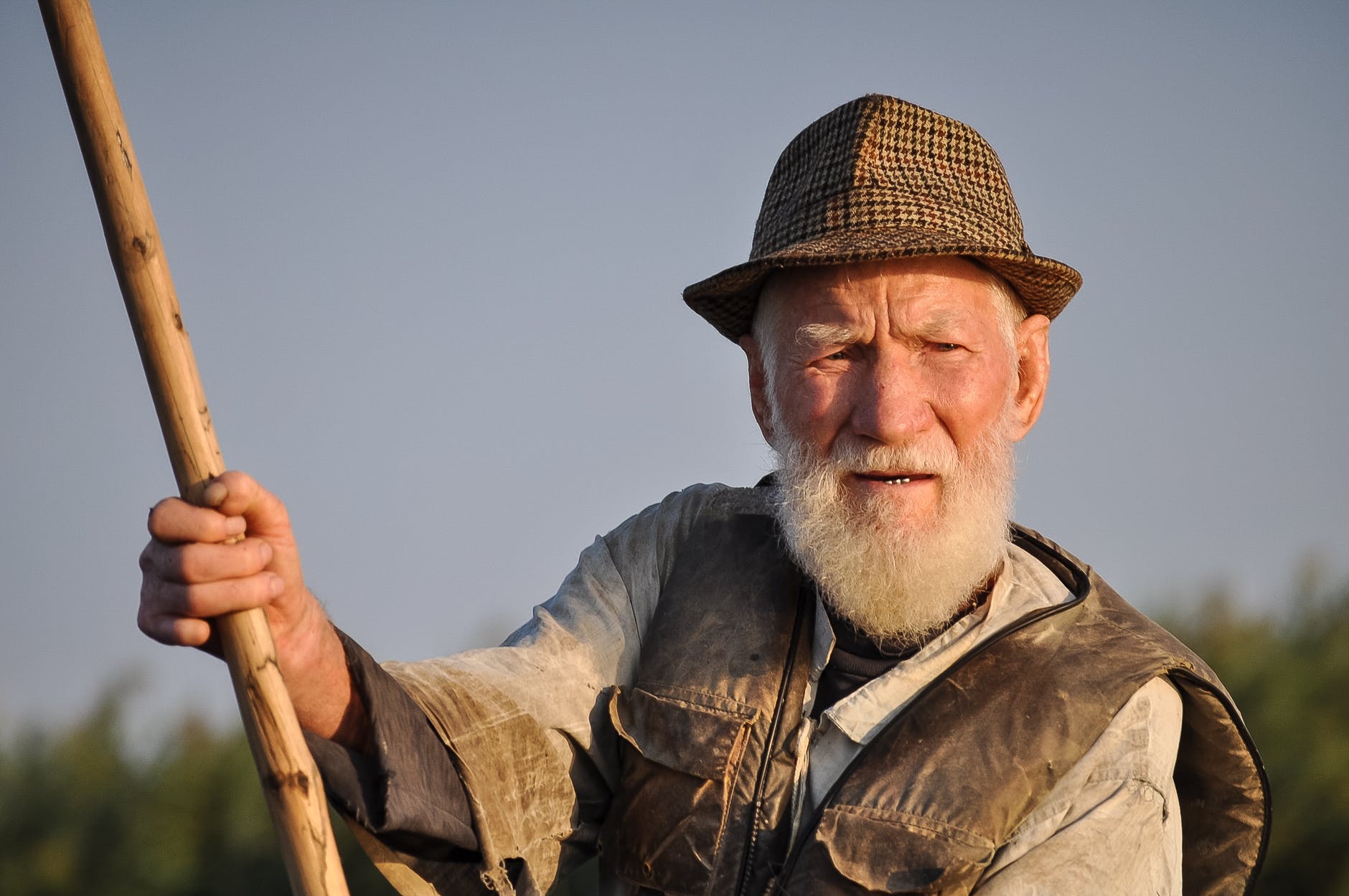 man wearing hat holding wooden rod under gray sky