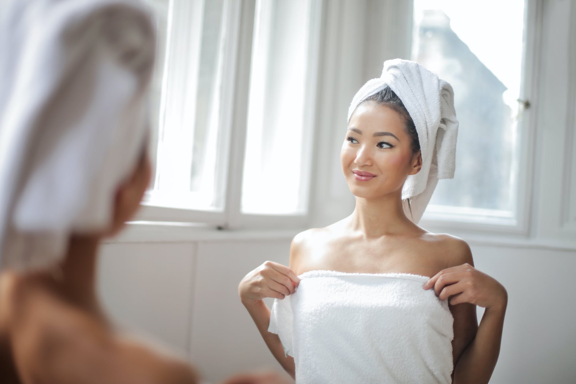 woman in white towel standing in front of the mirror